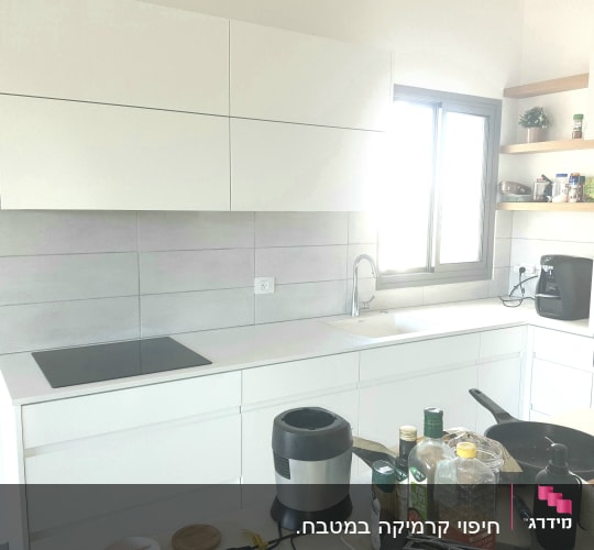 מטבח עם ארונות לבנים ומשטח עבודה, כיור וברז